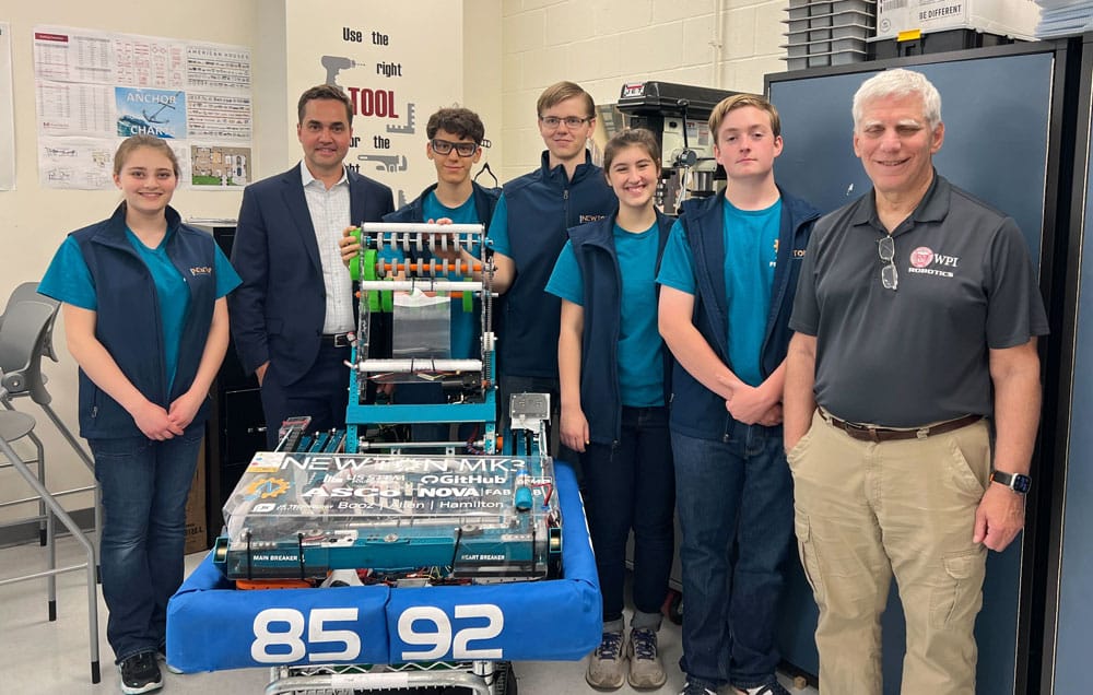 Brad Miller and David Rogers pose with team members from the FRC team Newton Squared in front of one of their robot builds.